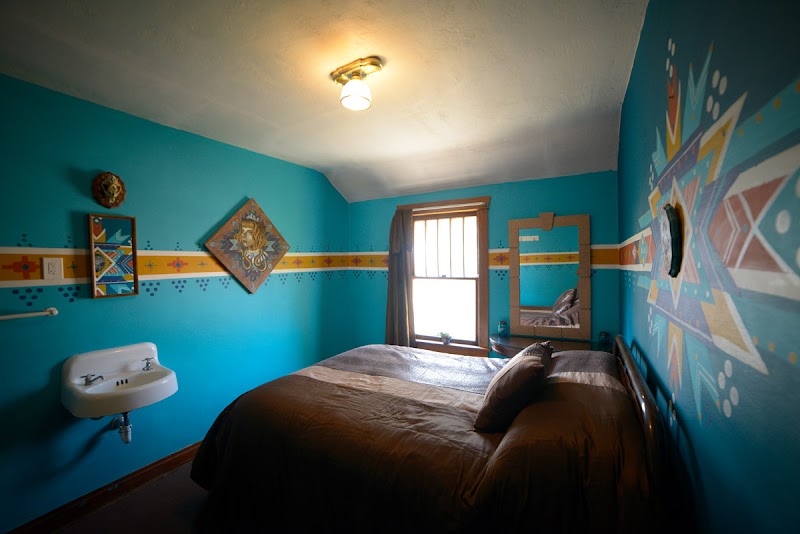 Turquoise bedroom with a brown bed, white wall sink, window with curtains, and bold geometric-tribal art in Arches National Park.