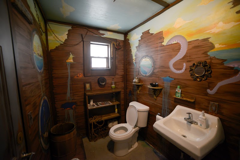 Rustic wooden bathroom with toilet, sink, small window, and painted desert mural in Arches National Park.