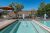 Poolside view with blue railing, orange umbrella, white chairs and tables, and desert hills near Arches National Park.