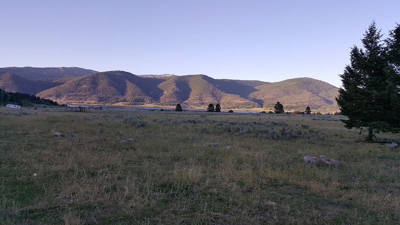 Grassy meadow at Watkins Creek Trailhead with distant mountains and a small trailer on the left in Yellowstone National Park.
