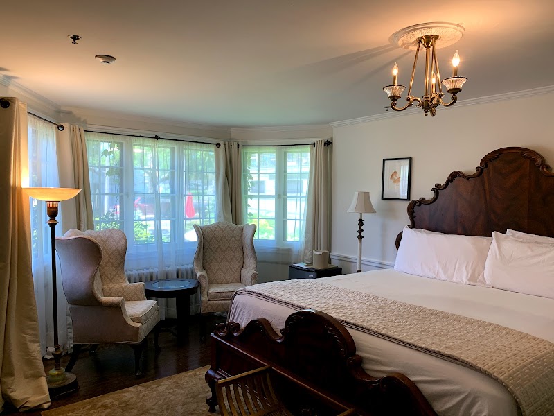 Comfortable hotel room interior at Acadia National Park's Village Center, featuring a carved wooden headboard bed and large bay windows.
