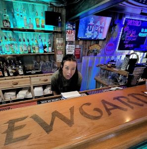 Interior of a bar in Yellowstone National Park with neon bottles, a bartender leaning toward the camera.
