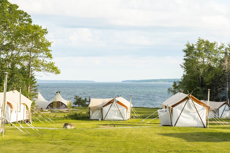 Coastal campground with white canvas tents arranged along the grassy shore of Acadia National Park, near the ocean.