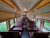 Interior of a vintage passenger train car with brown seats and a long aisle, windows reveal green woods, Acadia National Park.