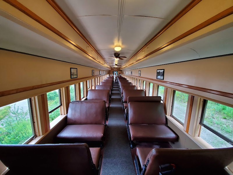 Interior of a vintage passenger train car with brown seats and a long aisle, windows reveal green woods, Acadia National Park.