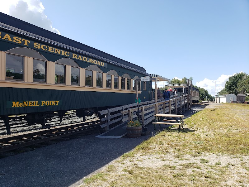Downeast Scenic Railroad cars at a platform along Acadia National Park, with a green railcar and wooden walkway