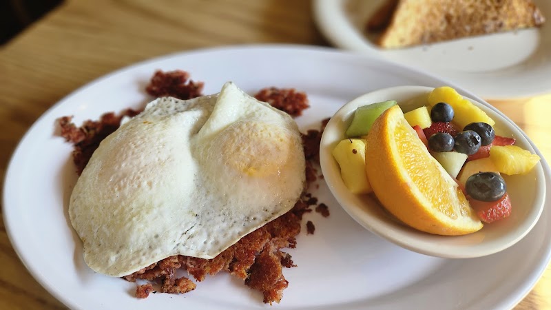 Breakfast plate with eggs benedict and a fruit cup at Bucksport waterfront in Acadia National Park, overlooking coastal scenery.
