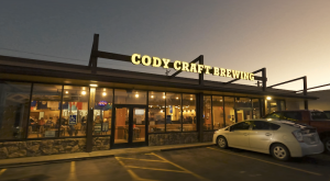 Cody Craft Brewing storefront in Yellowstone National Park at dusk, warm interior lights glow through large glass windows.