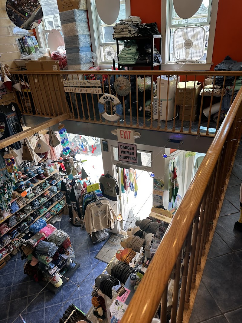 Interior view of Little Village Gifts shop in Acadia National Park, with shelves of shirts, hats and souvenirs along a blue-tiled floor.