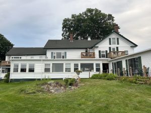 White, two-story lodge with attached wings, green shutters, wooden decks, and a manicured lawn at Acadia National Park.