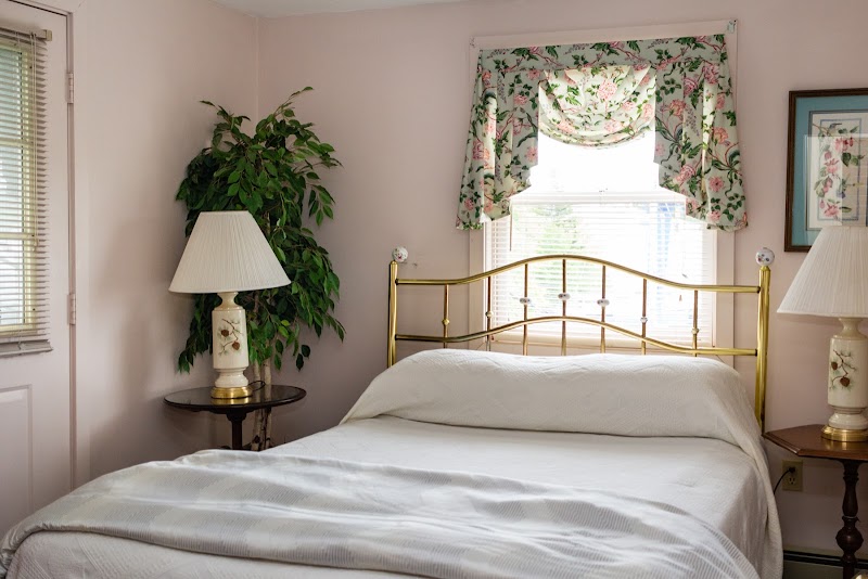Cozy bedroom with a brass headboard, white bedding, floral valance over the window, and two lamp-lit nightstands in Acadia National Park.