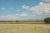 Badlands National Park landscape with open grassland, a distant fence, and rolling sandstone hills under a bright sky.