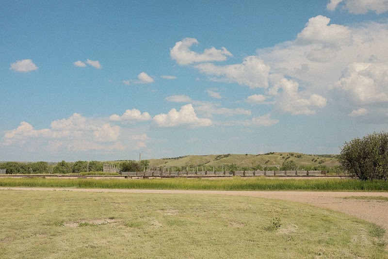 Grassy prairie with a low wooden fence, dirt path on the right, and rolling hills under a sky at Badlands National Park.