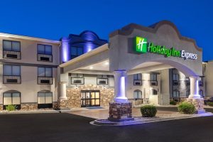 Exterior of a modern hotel with stone accents and blue-lit arches, parking lot, near Arches National Park.