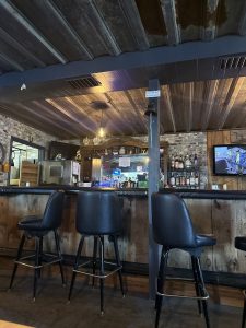 Rustic bar interior at Badlands National Park with wooden stools, brick walls, shelves of liquor, and a mounted TV.