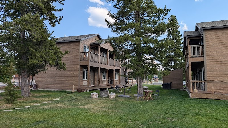 Two wooden lodge buildings with upper balconies overlook a grassy yard with pine trees in Yellowstone National Park.