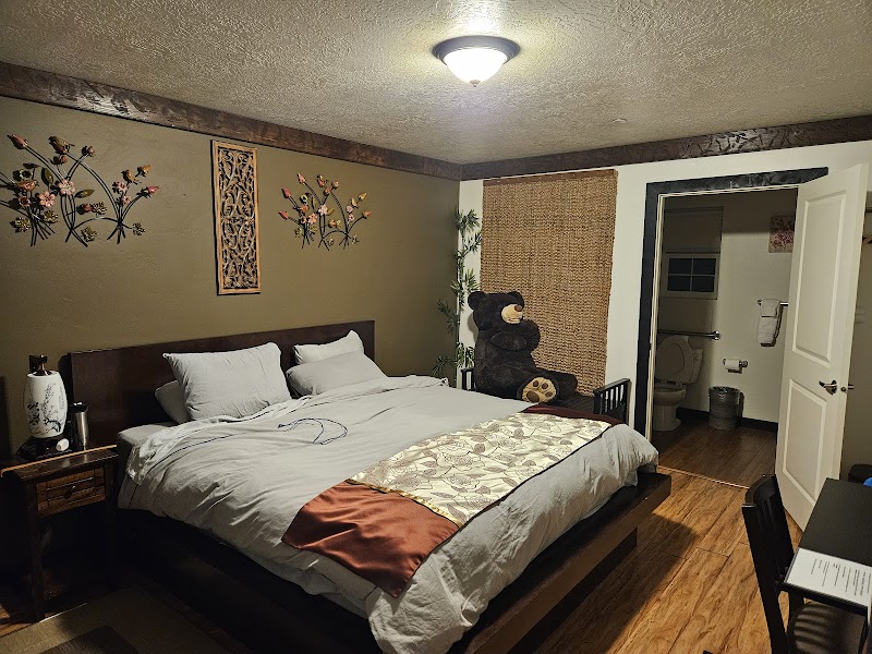 Cozy Yellowstone National Park bedroom with a large bed, grey linens, orange accent, wall art, a bear plush, and an open bathroom door.