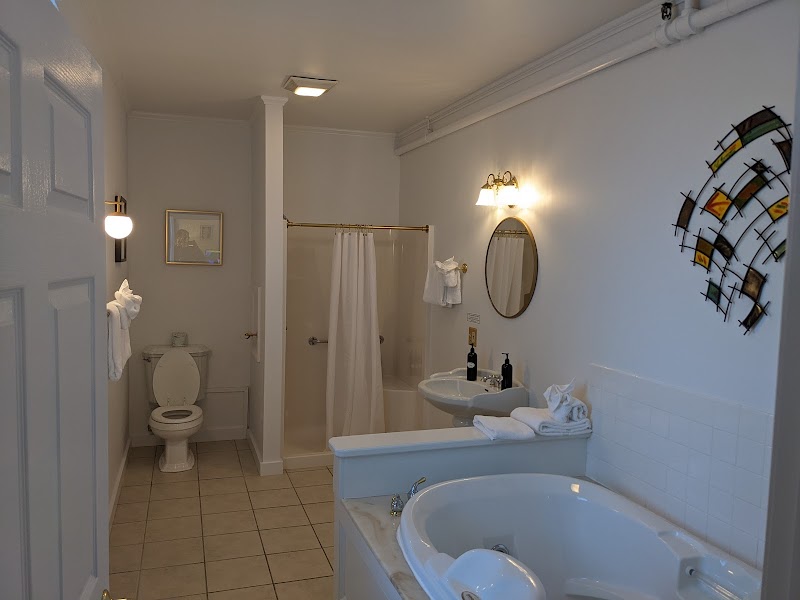 Spacious bathroom with a large white soaking tub, shower, toilet, sink, towels, oval mirror, and colorful wall art in Acadia.