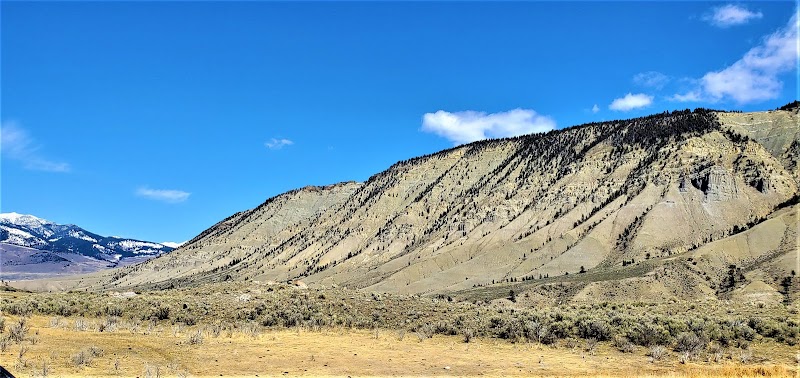 Sagebrush flats meet a ribbed canyon ridge and distant snow-capped peaks under a clear blue sky in Yellowstone National Park.