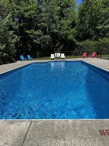 Acadia National Park campground swimming pool with bright blue water, surrounded by trees and colorful lounge chairs.