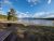Yellowstone National Park: wooden picnic table beside a lone tree, calm lake, and distant mountains under a blue sky.