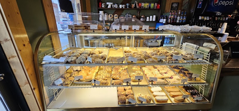 Curved glass bakery display in a Yellowstone National Park shop, with croissants, pastries, donuts and cookies on lit trays.