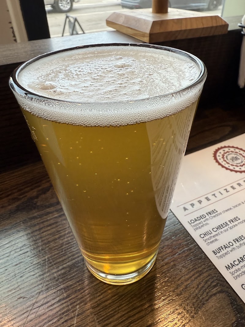Tall glass of pale beer with a frothy head on a dark wooden table, menu nearby, inside Arches National Park