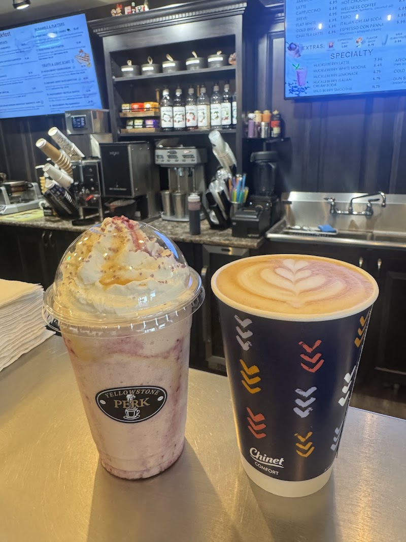 Milkshake topped with whipped cream and caramel drizzle beside a latte in a dark cafe at Yellowstone National Park.