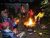 Group of campers seated in folding chairs around a glowing campfire at a wooded campground in Acadia National Park.