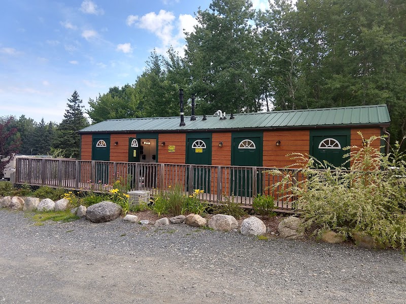 Wood-framed cabin with green doors and a railing sits on a gravel lot at Acadia National Park campground.