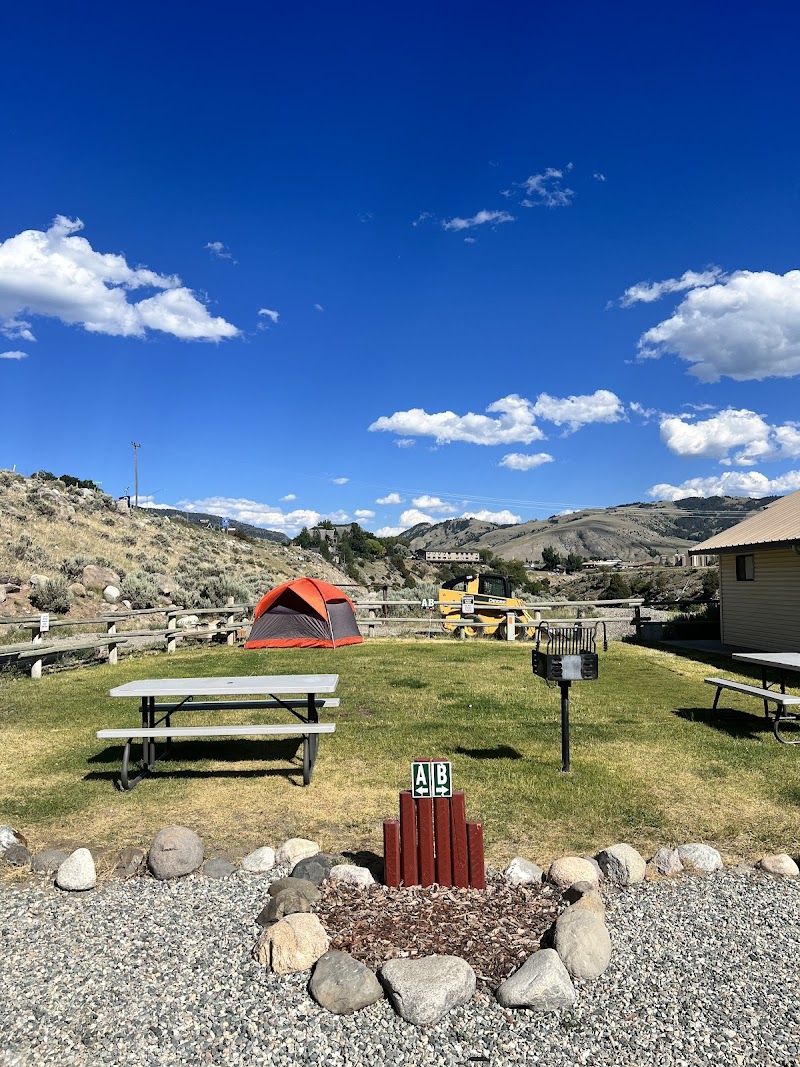 Bright orange tent on a grassy Yellowstone National Park campground, with picnic tables, a grill, and distant rolling hills.