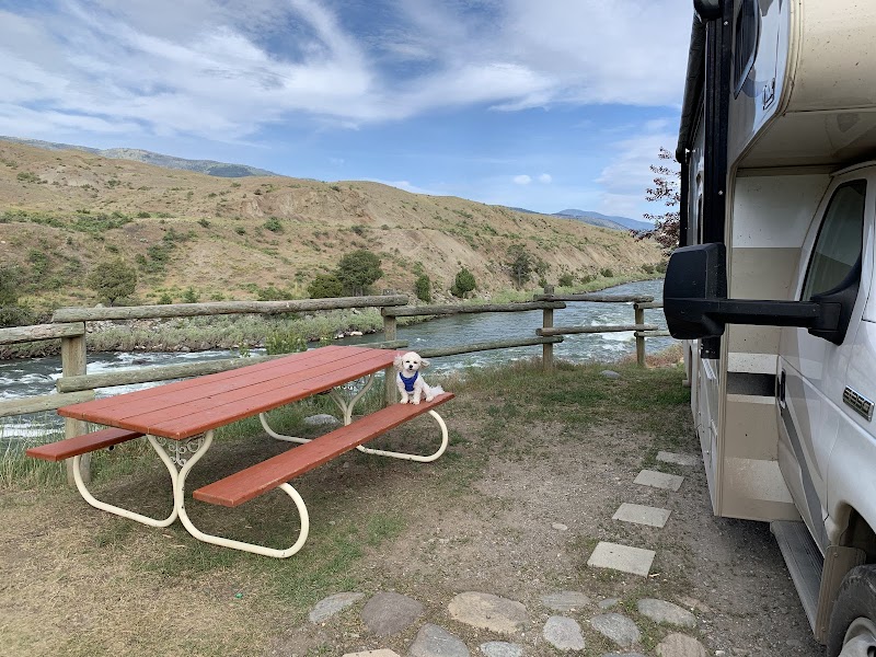 RV beside a red picnic table and wooden railing overlooking a fast river and brown hills in Yellowstone National Park.