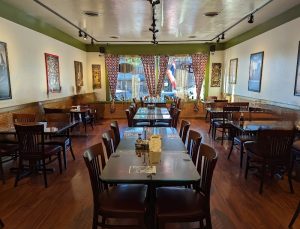 Cozy dining room with wooden tables and chairs, red patterned curtains, framed art, and warm lighting in Arches National Park.