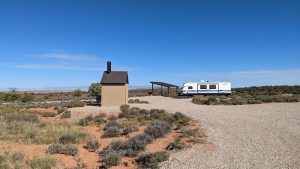 Arches National Park campground features a beige shed, a shelter, and a white travel trailer amid desert shrubs.