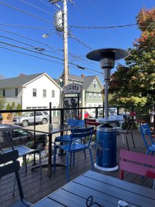 Outdoor deck seating with blue and pink chairs, a tall patio heater, and a view of town houses near Acadia National Park.