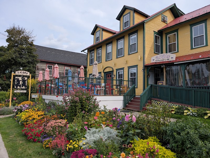 Yellow building with green trim hosts an outdoor patio with umbrellas, colorful tables, and a vibrant garden in Acadia National Park.