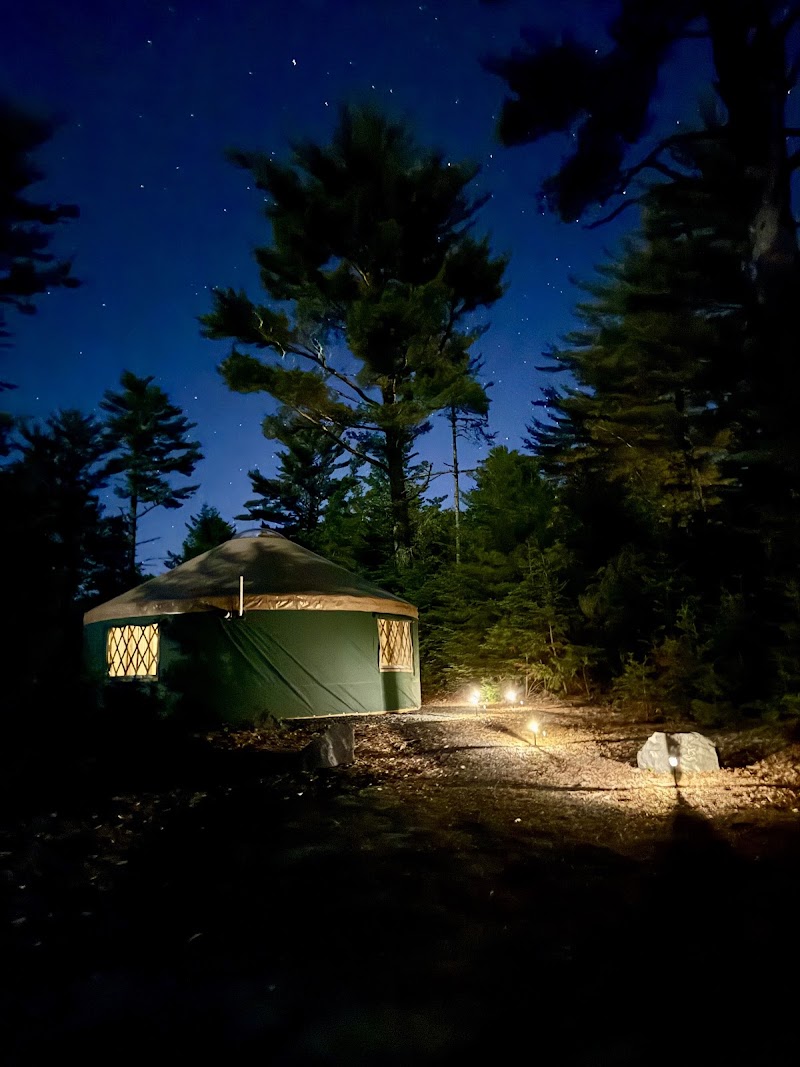 Night scene of a green canvas yurt at Evergreen Yurts campground in Acadia National Park, softly lit by campfire under a starry sky.