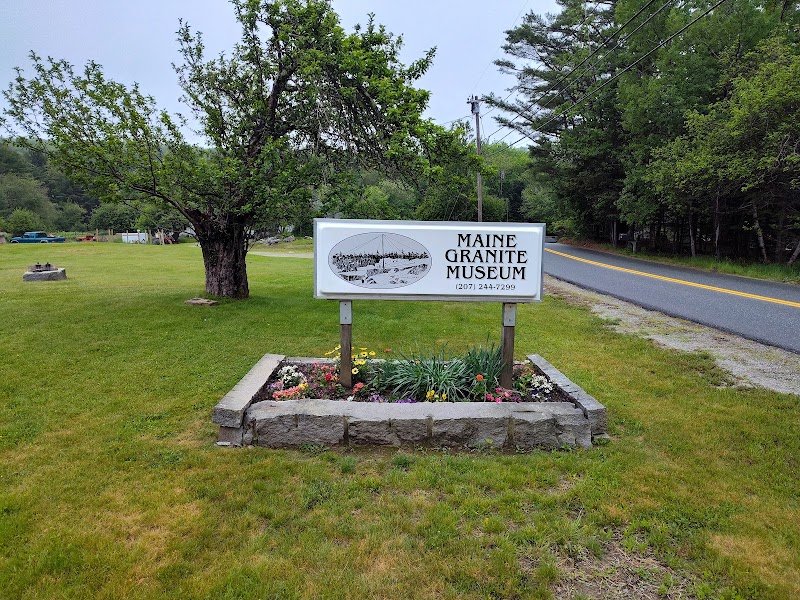 Granite industry sign along a roadside in Acadia National Park, framed by trees and a flower bed.