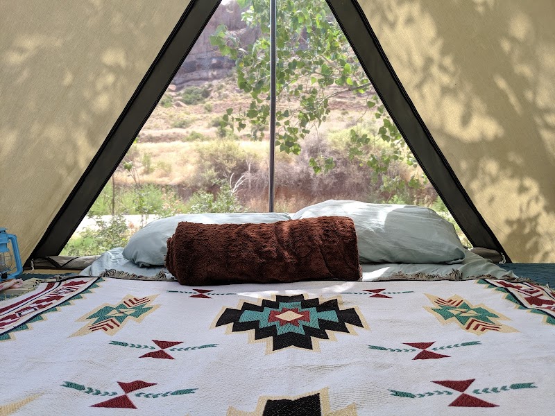 Cozy tent interior with a geometric quilt, two pillows, and desert vegetation visible through a triangular window at Arches NP.