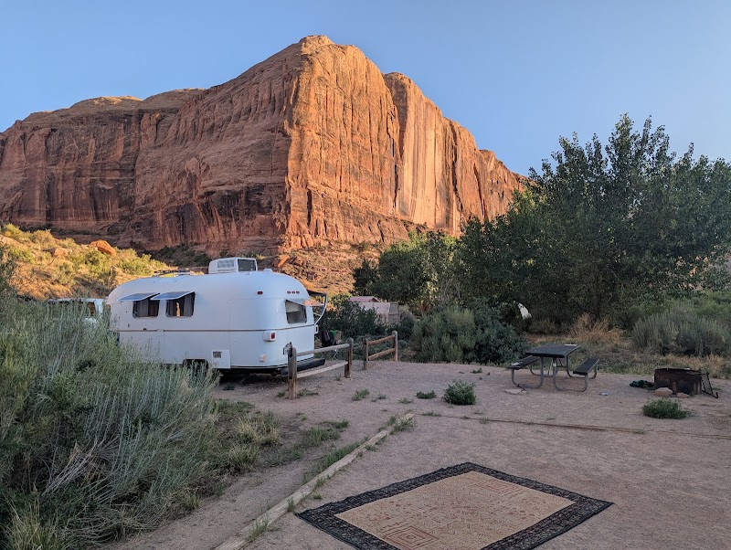 Sunlit white vintage camper trailer at a desert campground with a picnic table and fire pit near Arches National Park.