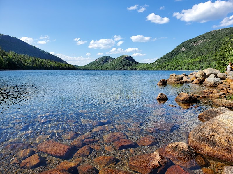 Jordan Pond Path Trailhead at Acadia National Park, showing clear lake, rocky shoreline, and forested mountains in the distance.