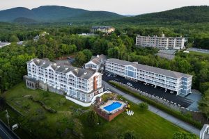 White and gray resort buildings surround a rectangular blue pool, bordered by green lawns and forested hills in Acadia National Park.