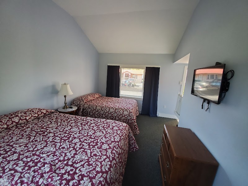 Two queen beds with red floral bedspreads, blue walls, window with dark curtains, wall-mounted TV, and wooden dresser in Acadia National Park.