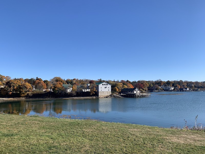 Calm Acadia National Park harbor with colorful autumn trees lining white and gray cottages along the water.