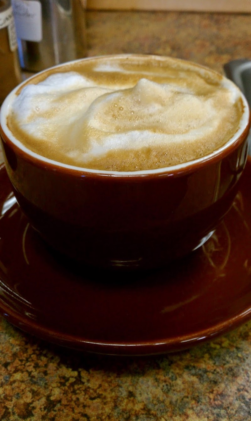 Foamy latte in a brown ceramic cup with saucer, rested on a speckled countertop at Arches National Park.