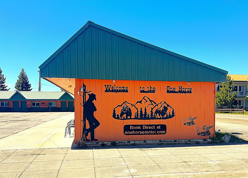 Orange motel building with a cowboy silhouette and mountain graphic, blue roof, in a parking lot at Yellowstone National Park.