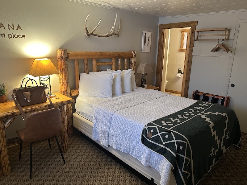 Rustic Yellowstone National Park room with a log bed, white linens, antler wall decor, warm lamps, and a wooden desk.