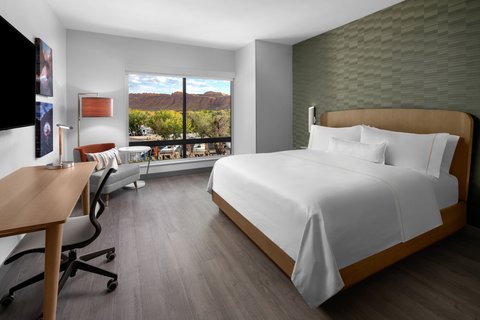 Hotel room at Arches National Park with a king bed, desk, chair, and a large window overlooking red rock cliffs.