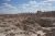 Rugged Badlands National Park terrain with layered eroded buttes, gullies, and sparse vegetation under a blue sky.
