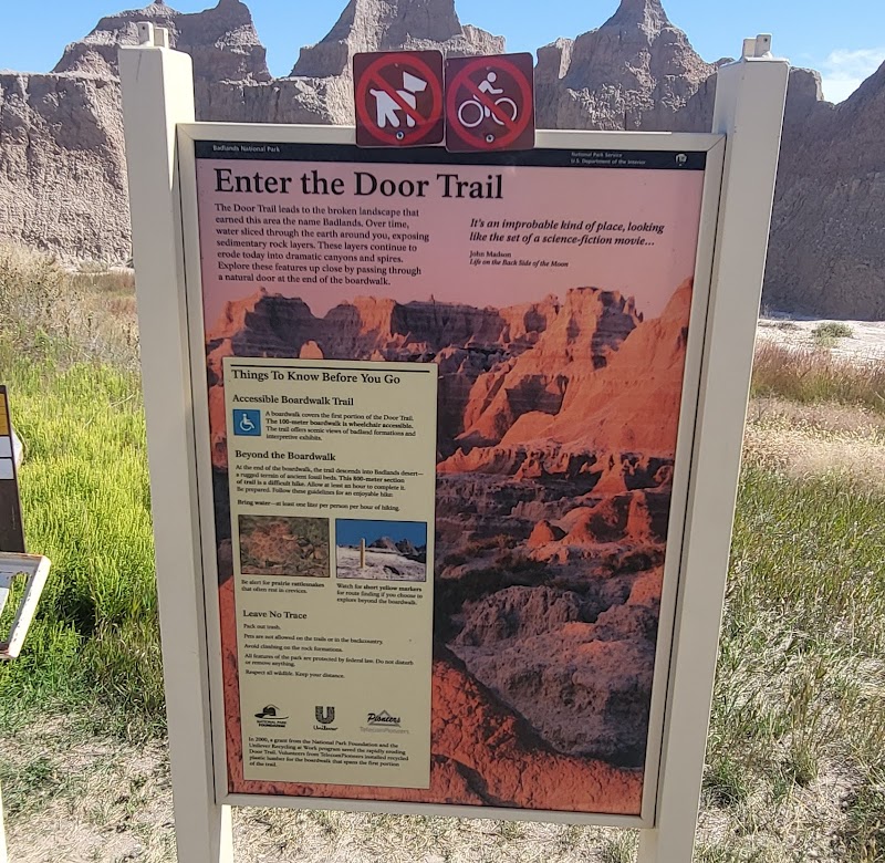 Signboard for the Door Trail at Badlands National Park, featuring a large image of eroded red rock formations in the background.